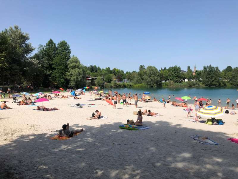 La plage de la base de loisirs Les O Kiri est recouverte sable. Des personnes se baignent dans le lac près de Lourdes