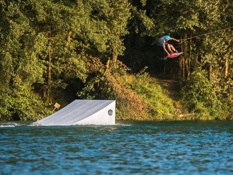 un homme faisant du téléski nautique et effectuant une figure dans les airs au dessus d'un lac près de Lourdes